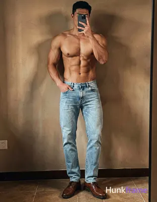 A handsome, muscular man leaning against a wall with one arm resting on it and the other hand in his