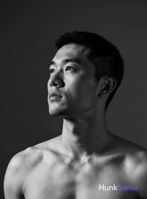 A handsome Asian man with a short black buzz cut and light stubble gazes upward 