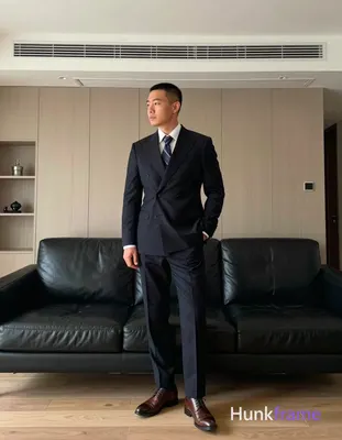 Asian man with short black buzz cut and clean-shaven face stands upright leaning against a black lea