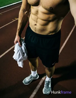 High-angle POV fashion editorial shot of a handsome adult man standing on an outdoor running track a