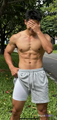 Asian man with tanned skin and short black hair stands on green grass near a paved path under trees.