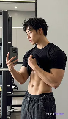 Asian adult man with short dark tousled hair and slight chin stubble stands in p