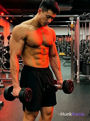 muscular male fitness model standing with dumbbells in hand, torso leaned forward slightly, well-def
