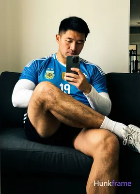 Asian man with light-medium skin and black short styled hair sits on a dark sofa
