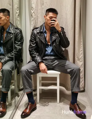 Asian man with short black buzz cut and light stubble sits on a white stool in an indoor dressing ro