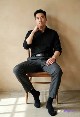 Adult man with short black hair and clean-shaven face sits in a wooden chair, leaning back against a