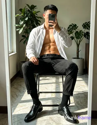 Seated on a black metal-framed chair with legs crossed, right leg over left knee