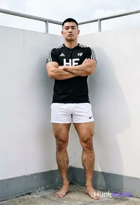 Asian man with short black buzz cut and clean-shaven face, standing leaning agai