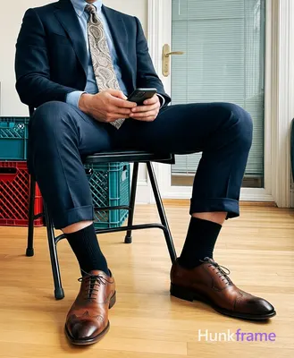 Waist-down shot of an adult man seated on a black folding chair, legs spread wide with knees bent an