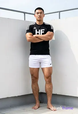 Asian man with short black buzz cut and clean-shaven face, standing leaning agai