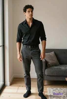 A handsome adult man with short black hair and clean-shaven face stands casually in a modern apartme
