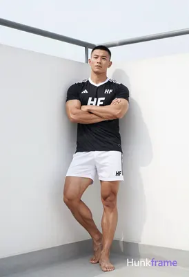 Asian man with short black buzz cut and clean-shaven face, standing leaning agai