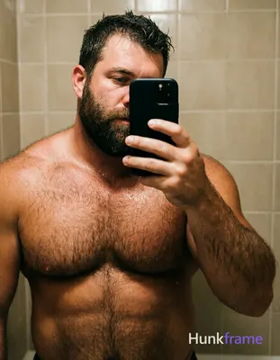A big hairy stocky masculine man stands shirtless in an indoor bathroom or showe