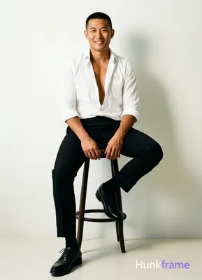 Asian man with short black buzz cut and clean-shaven face, medium-tan skin tone seated on tall stool