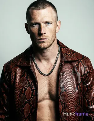 A handsome white man with fair freckled skin and short dark cropped hair stands head-and-shoulders c