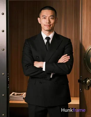 Asian man with buzz cut and light stubble on upper lip, gentle closed-mouth smile standing upright a