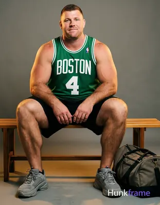 A stocky white man with short brown hair and a clean-shaven face sits on a wooden bench, legs spread