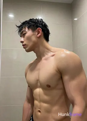 Asian man with short black hair slightly wet and glistening He stands shirtless in an indoor bathroo