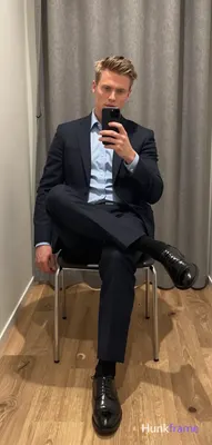 Seated on a chair with metal legs and black cushion, left leg extended forward, right knee bent and 