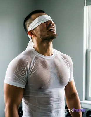 Asian man with short black buzz cut and light stubble stands upright in a home g