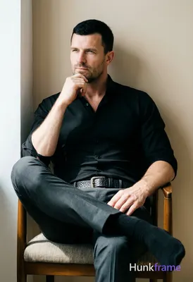 A handsome adult man with short black hair and clean-shaven face sits centered in a vertical portrai