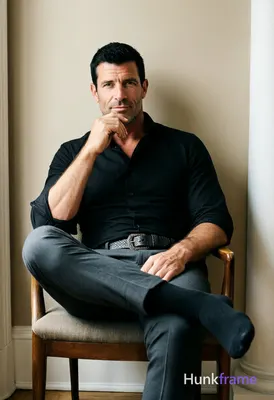 A rugged adult man with short black hair and clean-shaven face sits centered in 