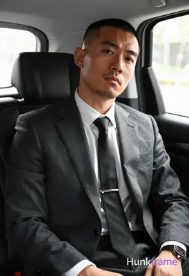 Asian man with buzz cut and light stubble seated upright in a luxury vehicle bac