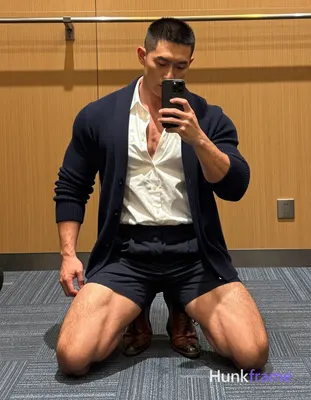 A rugged muscle bear with medium-brown skin and a black buzz cut kneels on blue-