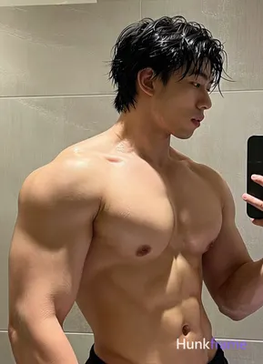 Asian man with short black hair slightly wet and glistening He stands shirtless in an indoor bathroo