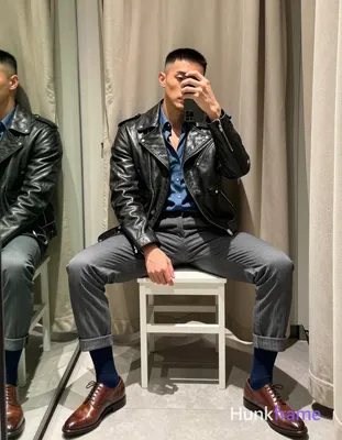 Asian man with short black buzz cut and light stubble sits on a white stool in an indoor dressing ro