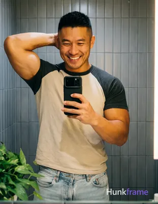 Asian man with short black buzz cut and high fade stands in front of a bathroom 