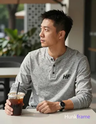 He wears a grey long-sleeve henley shirt with three-button placket, seated at outdoor café table ang