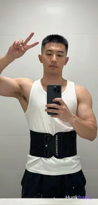 Asian man with short black buzz cut and clean-shaven face, standing facing a bathroom mirror; He wea