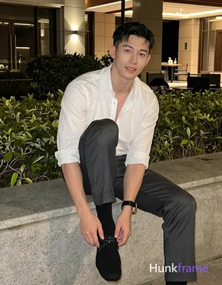Asian adult man with short dark straight side-parted hair and clean-shaven face, seated on stone led