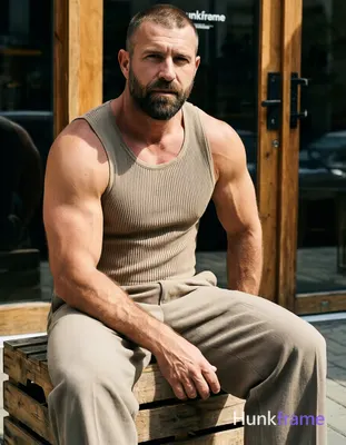 Seated adult man on wooden crate, torso angled right, left arm resting along thigh with hand near kn