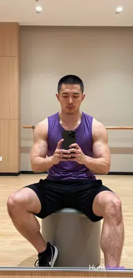 Asian man with short black buzz cut and light stubble sits centered in a gym mirror reflection on a 