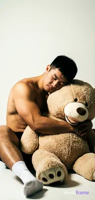Adult man with short black hair and clean-shaven face, eyes closed resting head on a large beige ted
