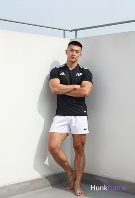 Asian man with short black buzz cut and clean-shaven face, standing leaning agai