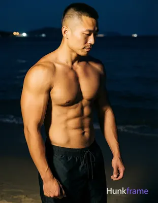 Asian man with short buzz cut and clean-shaven face stands upright in night beach setting, torso ang