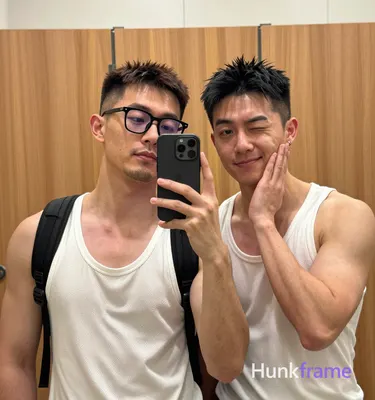 Two adult Asian men standing close together in a mirror selfie, left side of frame holding black sma