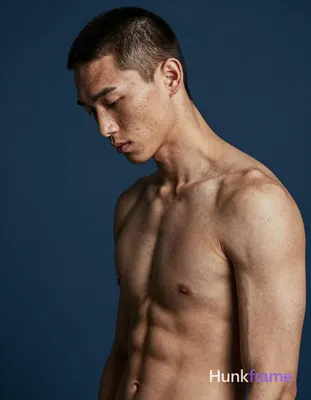 A white man with fair skin and freckles poses shirtless in a fine-art athletic p