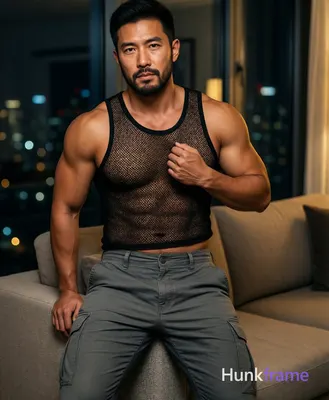 Asian man standing in modern apartment living room, leaning casually against sof