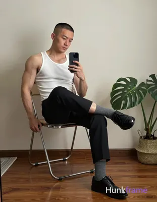 Asian man with short buzz cut and light-medium skin sits on a metal-framed chair, right leg crossed 