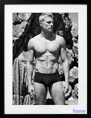 A handsome white man with short light-colored hair and clean-shaven face stands casually in a vertic