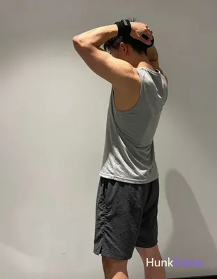 An athletic masculine man captured in gym photography, standing in profile with left arm raised behi
