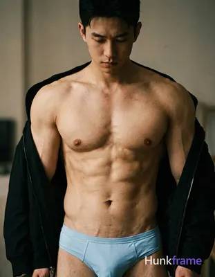 A shirtless man standing with his head slightly tilted forward, wearing a black 