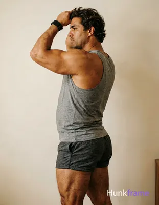 A big hairy stocky masculine man with bear energy, standing in profile with left arm raised behind h