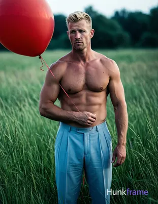 Adult man with light skin and short styled blonde hair stands shirtless in tall green grass, facing 