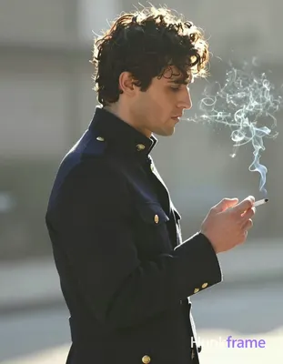 A handsome adult man with dark curly hair stands in right-side profile facing ri