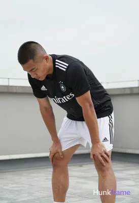 Asian man with short buzz cut and matte dark hair stands bent forward at waist, 